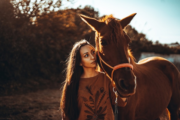 Кавказская женщина позирует с коричневой лошадью