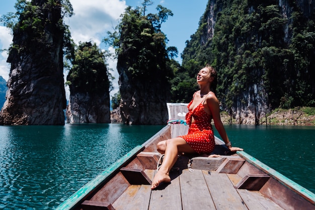 Caucasian woman in red summer dress on thai asian boat on vacation, travel around Thailand