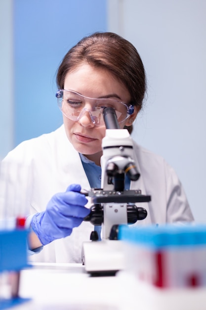 Caucasian woman scientist in white coat looking in high end microscope for pharmacy expertise