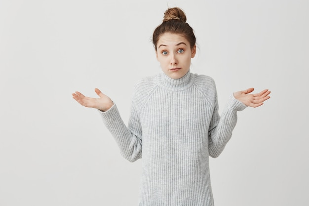 Caucasian woman throwing up hands with uncertainty on face. Female startup entrepreneur acting like have no idea or don't care over white wall. Emotions concept