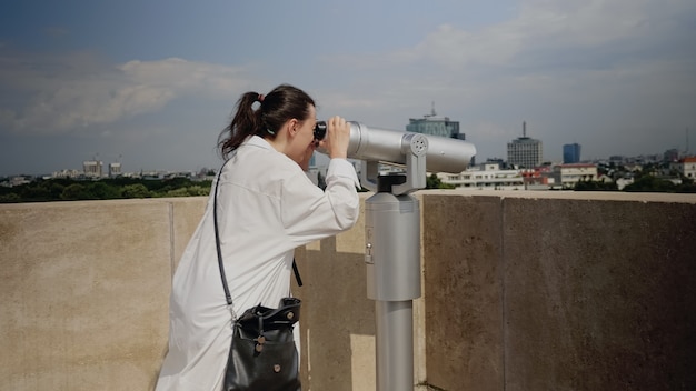 Free photo caucasian woman using telescope from observation point