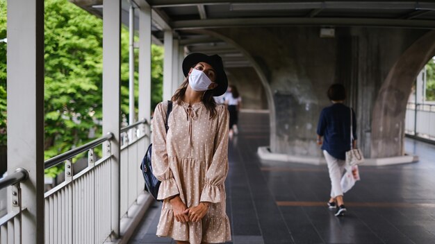 방콕 시내에서 유행병 동안 의료 얼굴 마스크에 지하철 교차점을 걷고 백인 여자.