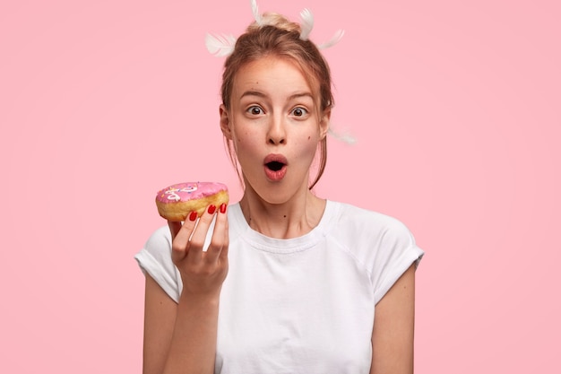 Caucasian woman with feathers in hair and holding donut