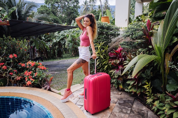 Кавказская женщина с большим розовым чемоданом на отдыхе в тропической стране
