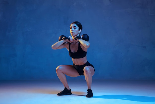 Caucasian young female athlete practicing on blue in neon light