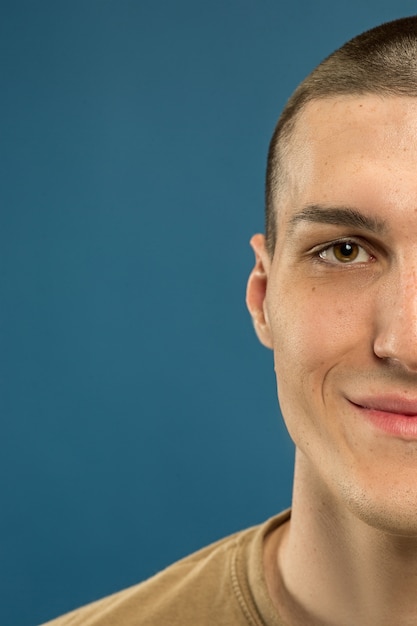 Free photo caucasian young man's close up shot on blue studio background. beautiful male model in shirt. concept of human emotions, facial expression, sales, ad. smiling, looks happy.