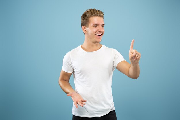 Caucasian young man's half-length portrait on blue studio background. Beautiful male model in shirt. Concept of human emotions, facial expression, sales, ad. Touching an empty search bar.