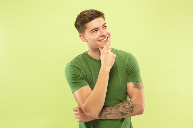 Поясной портрет кавказского молодого человека на фоне зеленой студии. Красивая мужская модель в рубашке. Понятие человеческих эмоций, выражения лица, продаж, рекламы. Вдумчивый и уверенный. Улыбается.