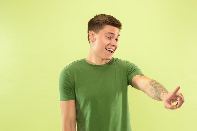 Caucasian young man's half-length portrait on green studio background. Beautiful male model in shirt. Concept of human emotions, facial expression, sales, ad. Touching empty space search bar.