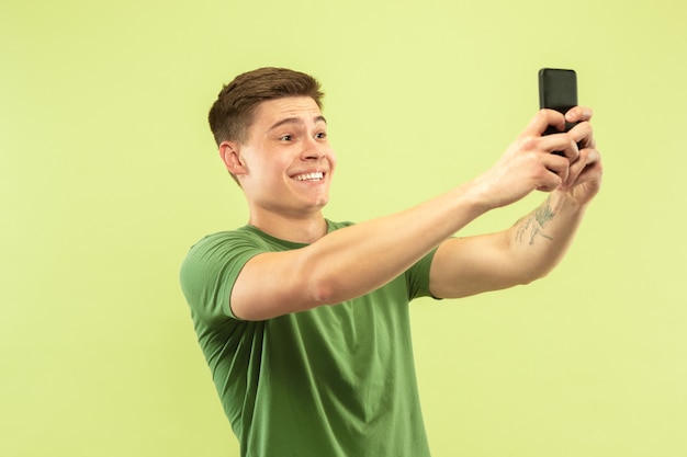 Caucasian young man's half-length portrait on green studio space. Beautiful male model in shirt