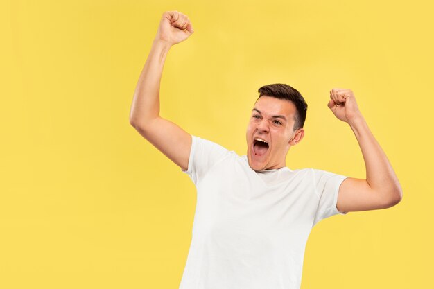 Caucasian young man's half-length portrait on yellow studio background. Beautiful male model in shirt. Concept of human emotions, facial expression, sales, ad. Celebrating, calling, screaming.