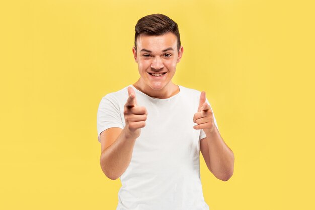 Caucasian young man's half-length portrait on yellow studio background. Beautiful male model in shirt. Concept of human emotions, facial expression, sales, ad. Pointing on and looks happy.
