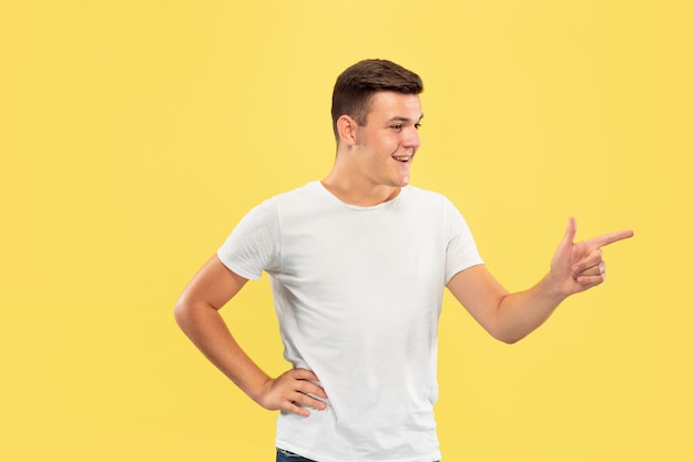 Ritratto a mezzo busto del giovane caucasico su sfondo giallo studio. bellissimo modello maschile in camicia. concetto di emozioni umane, espressione facciale, vendite, annuncio. indicando il lato, sembra felice.