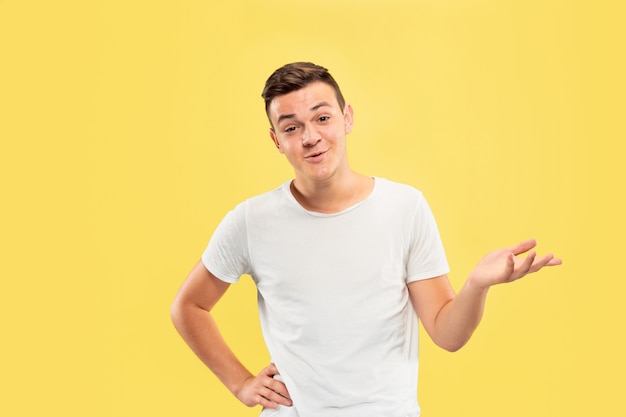 Caucasian young man's half-length portrait on yellow studio background. Beautiful male model in shirt. Concept of human emotions, facial expression, sales, ad. Showing something, copyspace.