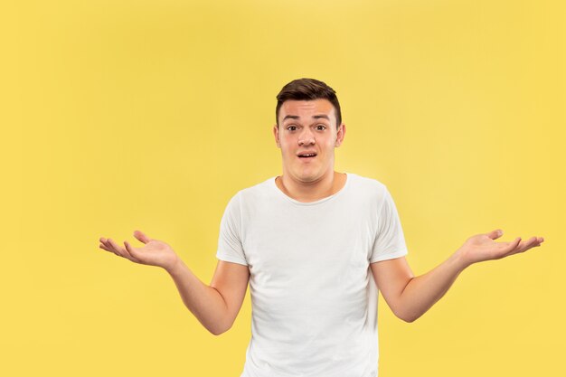 Caucasian young man's half-length portrait on yellow studio background. Beautiful male model in shirt. Concept of human emotions, facial expression, sales, ad. Showing something, looks uncertain.