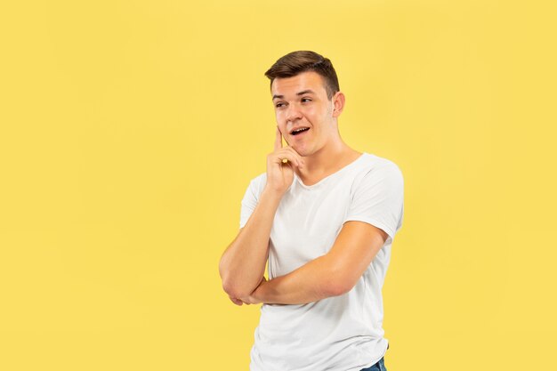 Caucasian young man's half-length portrait on yellow studio background. Beautiful male model in shirt. Concept of human emotions, facial expression, sales, ad. Thinking, having an idea, attented.