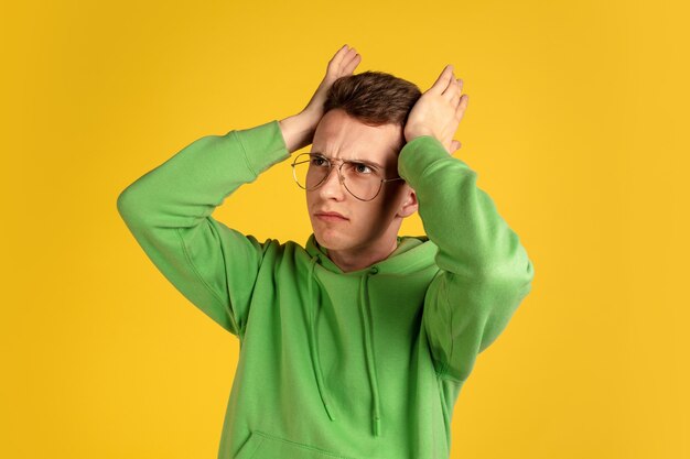 Caucasian young man's portrait on yellow  wall. Beautiful male model in green outfit gesturing. Concept of human emotions, facial expression, sales, ad, youth. Copyspace.