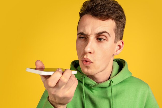 Caucasian young man's portrait on yellow  wall. Beautiful male model in green outfit gesturing. Concept of human emotions, facial expression, sales, ad, youth. Copyspace.