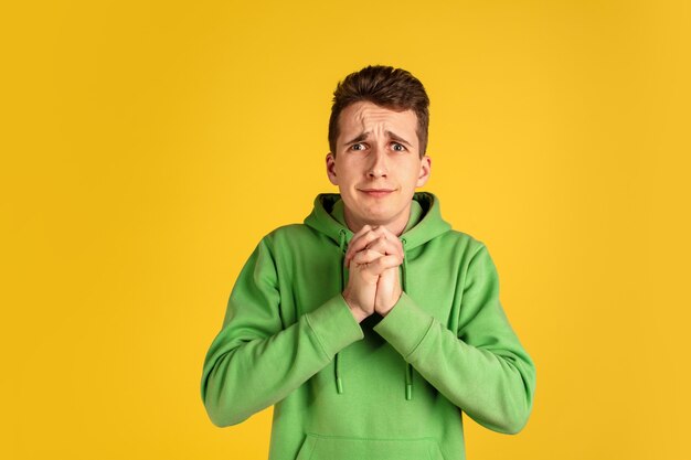 Caucasian young man's portrait on yellow  wall. Beautiful male model in green outfit gesturing. Concept of human emotions, facial expression, sales, ad, youth. Copyspace.