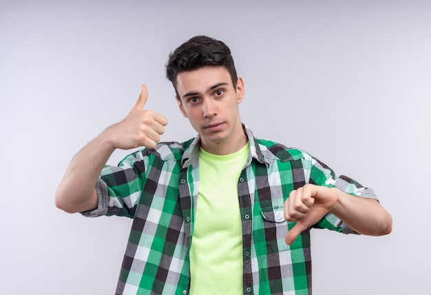 Кавказский молодой человек в зеленой рубашке, подняв большой палец вверх другой вниз на изолированной белой стене