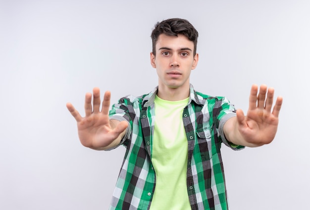 Бесплатное фото Кавказский молодой человек в зеленой рубашке показывает жест остановки обеими руками на изолированной белой стене