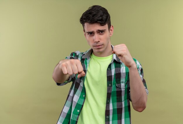 caucasian young man wearing green shirt standing in fighting pose on isolated green wall