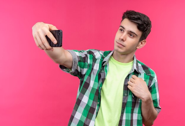 Caucasian young man wearing green shirt takes a selfie on isolated pink wall