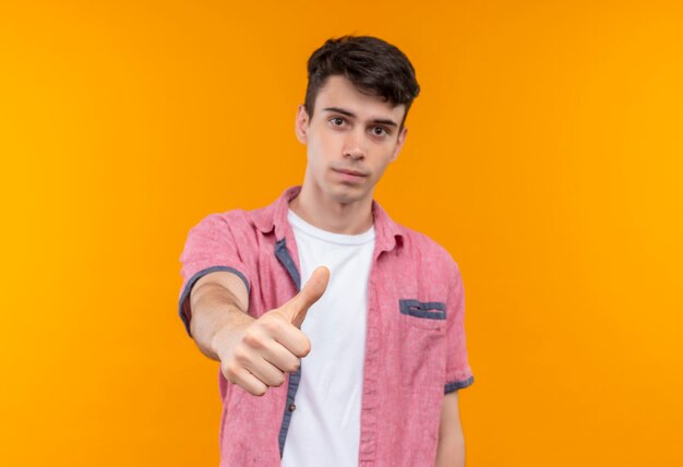 孤立したオレンジ色の壁に彼の親指をピンクのシャツを着ている白人の若い男