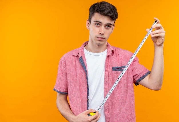 Free photo caucasian young man wearing pink shirt holding tape meter on isolated orange wall