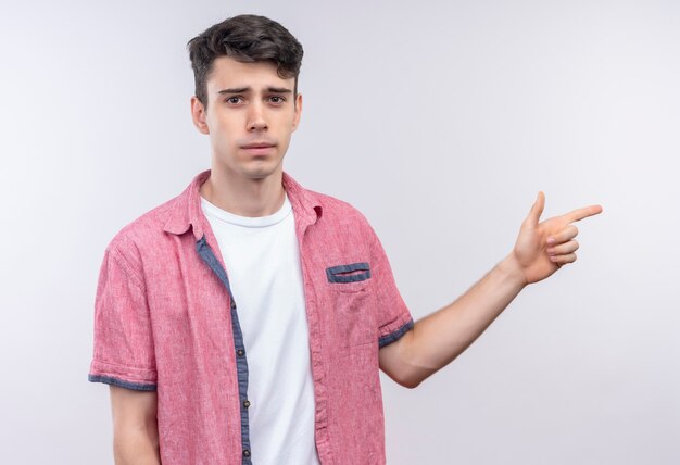 caucasian young man wearing pink shirt points to side on isolated white wall
