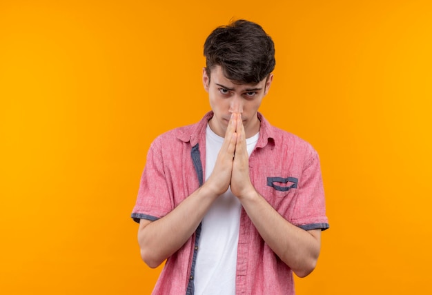 孤立したオレンジ色の壁に祈りのジェスチャーを示すピンクのシャツを着ている白人の若い男