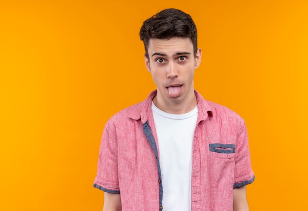 Caucasian young man wearing pink shirt showing tongue on isolated orange wall