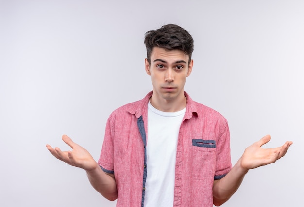 caucasian young man wearing pink shirt spreads hands on isolated white wall