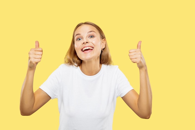 Caucasian young woman's half-length portrait on yellow studio background. Beautiful female model in white shirt. Concept of human emotions, facial expression. Showing the sign of nice, cool.