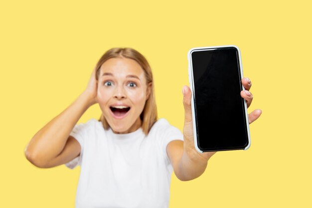 Caucasian young woman's half-length portrait on yellow studio background. Beautiful female model in white shirt