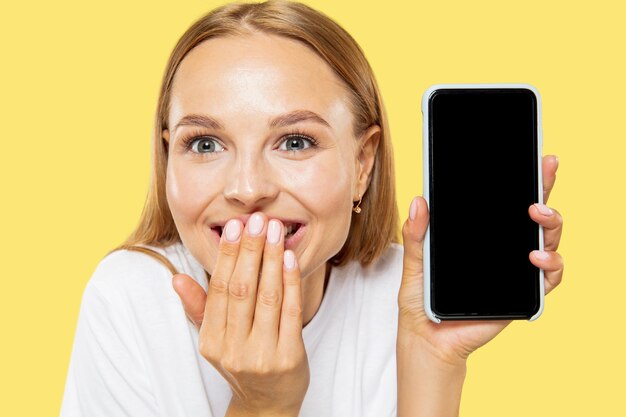 Caucasian young woman's half-length portrait on yellow studio background. Beautiful female model in white shirt