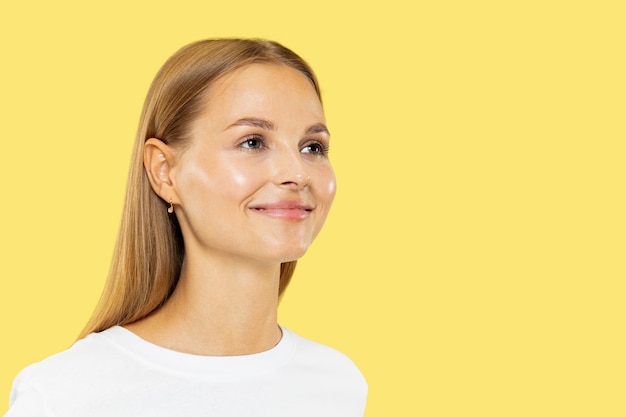 Caucasian young woman's half-length portrait on yellow studio background. Beautiful female model in white shirt