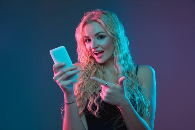 Caucasian young woman's portrait on gradient background in neon light. Beautiful female model with unusual look. Concept of human emotions, facial expression, sales, ad. Making selfie, bet, purchases.