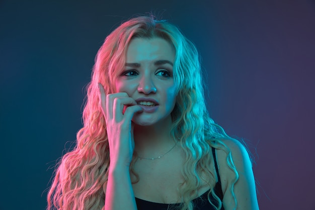 Caucasian young woman's portrait on gradient background in neon light. Beautiful female model with unusual look. Concept of human emotions, facial expression, sales, ad. Scared, thoughtful.