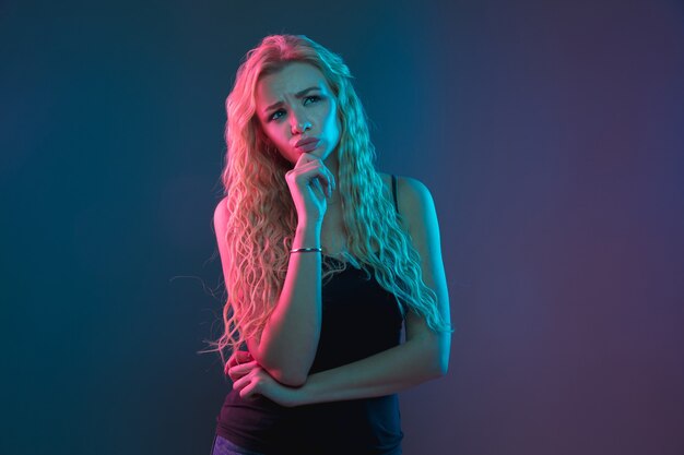 Caucasian young woman's portrait on gradient background in neon light. Beautiful female model with unusual look. Concept of human emotions, facial expression, sales, ad. Thoughtful, dreamful.