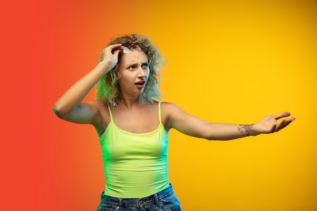 Caucasian young woman's portrait isolated on gradient studio background in neon. Beautiful female curly model in casual style. 