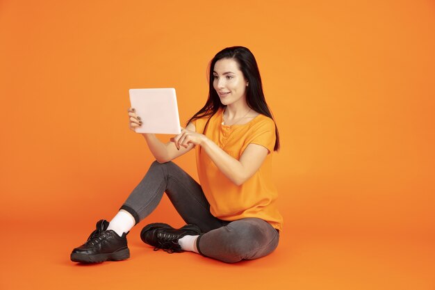 Caucasian young woman's portrait on orange  space. Beautiful female brunette model in shirt