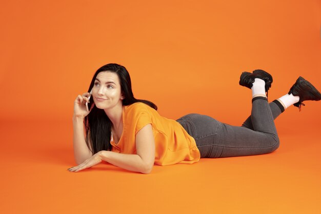 Caucasian young woman's portrait on orange  space. Beautiful female brunette model in shirt