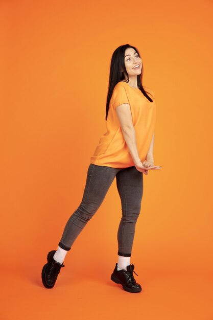 Портрет молодой женщины Кавказа на оранжевом фоне студии. Красивая женская модель брюнет в рубашке. Понятие человеческих эмоций, выражения лица, продаж, рекламы. Copyspace. Танцы, смех.