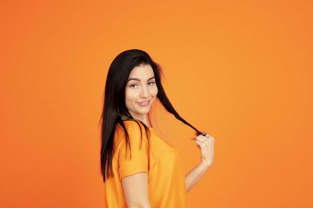 Портрет молодой женщины Кавказа на оранжевом фоне студии. Красивая женская модель брюнет в рубашке. Понятие человеческих эмоций, выражения лица, продаж, рекламы. Copyspace. Выглядит мило, улыбается.