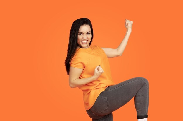 Caucasian young woman's portrait on orange studio background. Beautiful female brunette model in shirt. Concept of human emotions, facial expression, sales, ad. Copyspace. Win like winner, laughting.