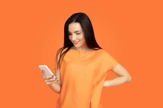 Caucasian young woman's portrait on orange studio background.