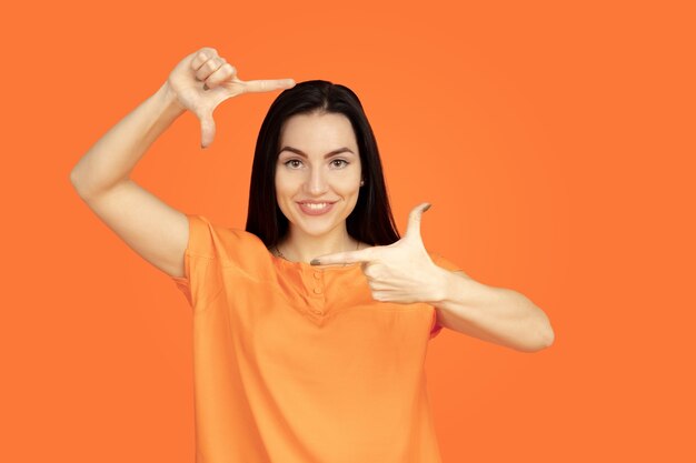 Caucasian young woman's portrait on orange studio background.