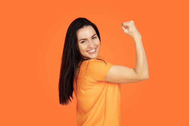 Caucasian young woman's portrait on orange studio background.