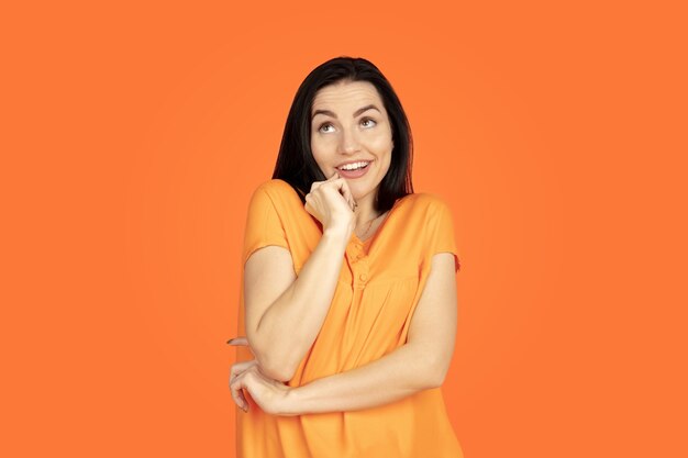 Caucasian young woman's portrait on orange studio background.